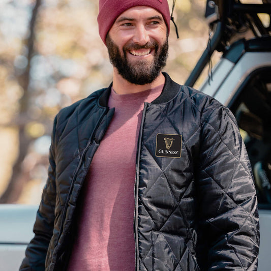 A bearded man wearing a waterproof black Guinness Quilted Utility Zip Up jacket and beanie.