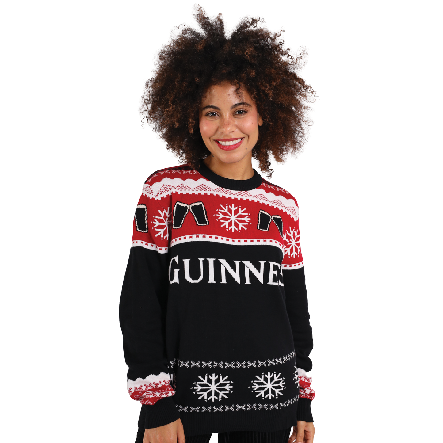 A woman with curly hair smiles while wearing the Official Guinness Holiday Sweater, a black, red, and white knit by Guinness featuring festive snowflake and pint glass designs.