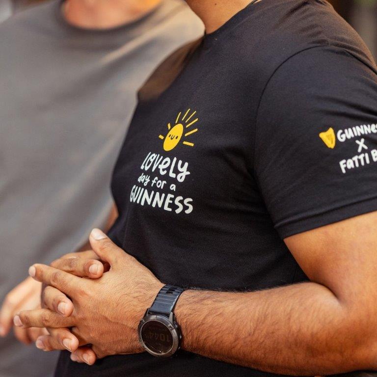 Two men wearing FATTI BURKE "LOVELY DAY FOR A GUINNESS" BLACK TEE with a smile on them, enjoying the summer weather.