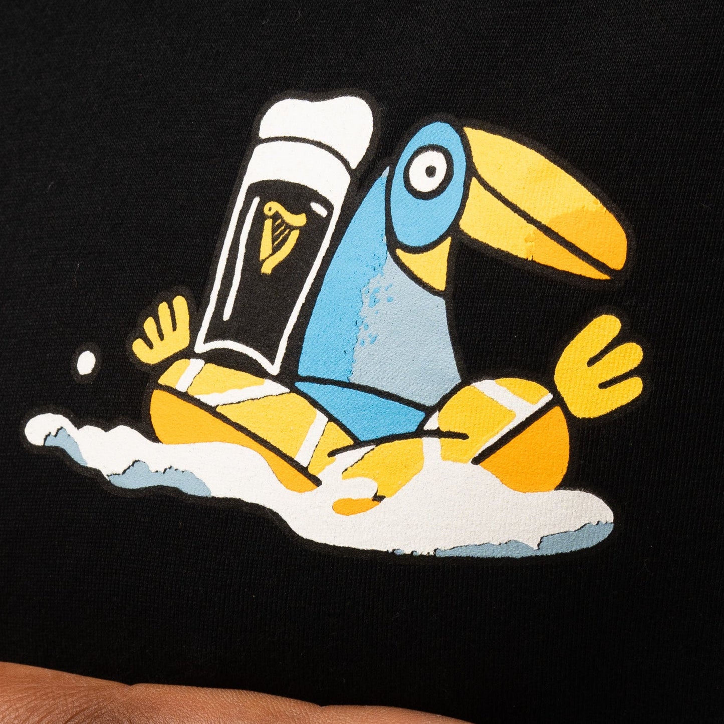 Illustration of a blue and yellow toucan with a pint of Guinness, inspired by Sebastian Curi, on the black Guinness Seb Curi Oversize Tee from Guinness Webstore US.