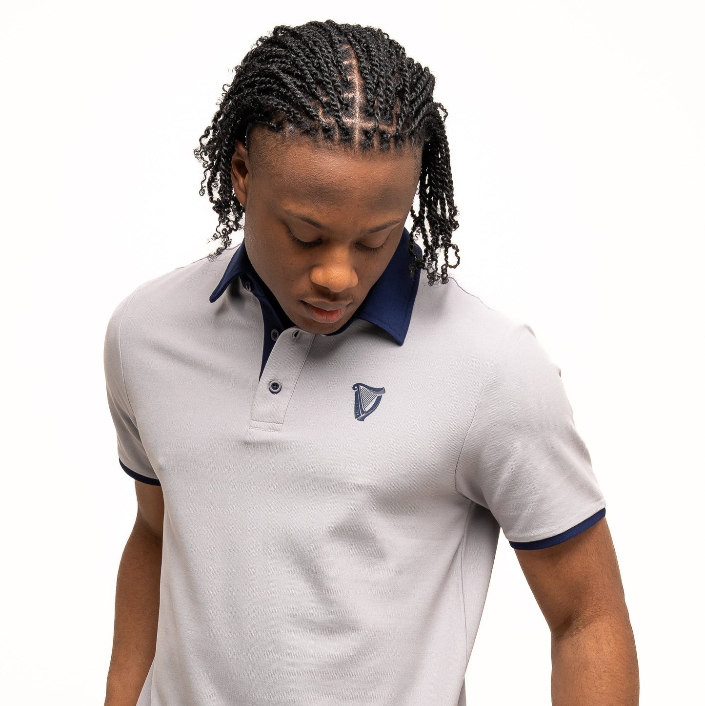 A person wearing the Guinness Performance Polo - Grey from Guinness Webstore US, featuring dark navy trim and crafted from premium double pique fabric, looks down while holding the shirt’s hem against a plain white background.