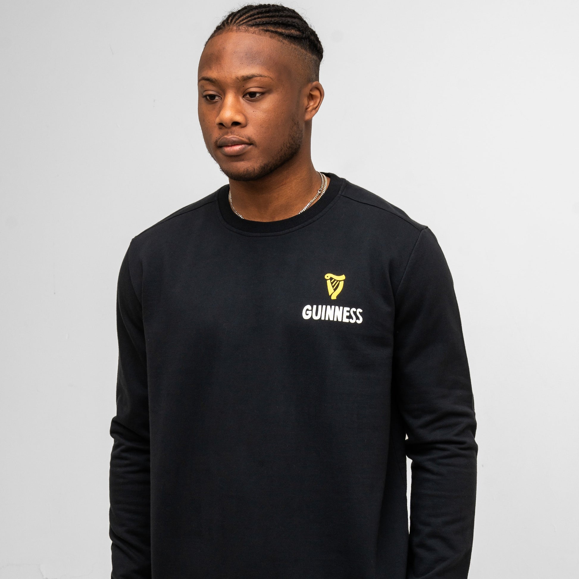 A man wears the Guinness Seb Curi Lovely Day Sweatshirt in black from Guinness Webstore US, standing against a plain light gray background.