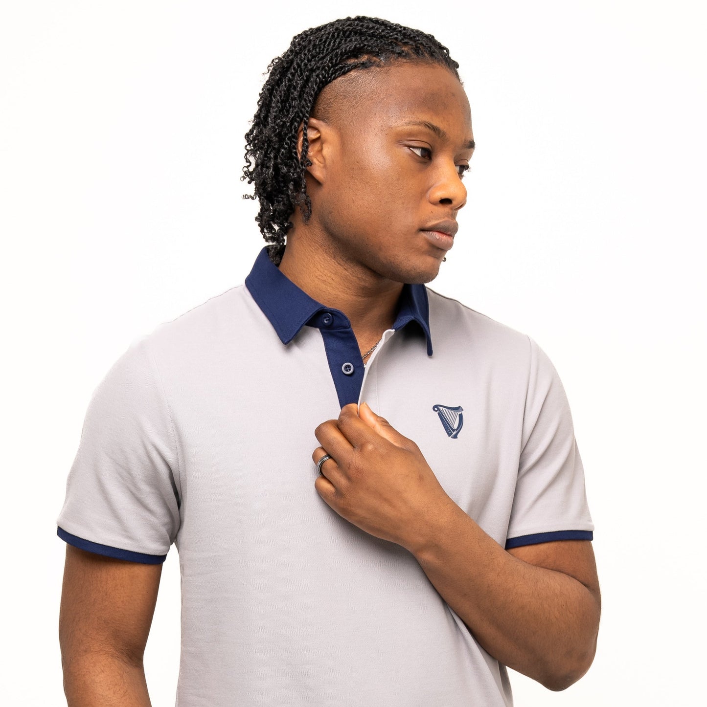 A person in the Guinness Webstore US Guinness Performance Polo - Grey, featuring a dark collar and sleeve edges, stands against a white background, looking sideways with one hand near the collar of this premium double pique fabric shirt.