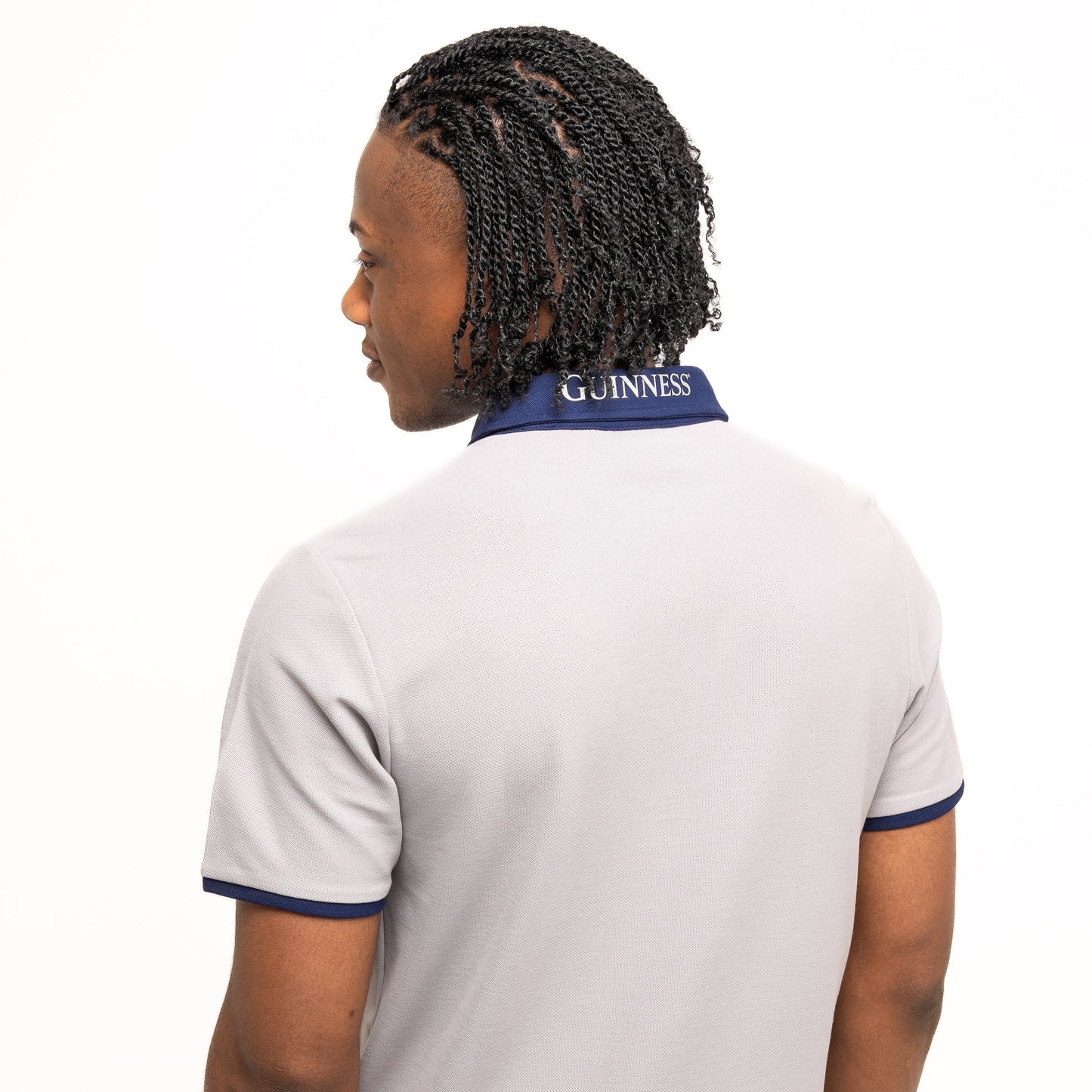 A man faces away from the camera wearing the Guinness Performance Polo - Grey from Guinness Webstore US, featuring navy trim and "GUINNESS" on the back collar—showcasing stylish golf apparel.