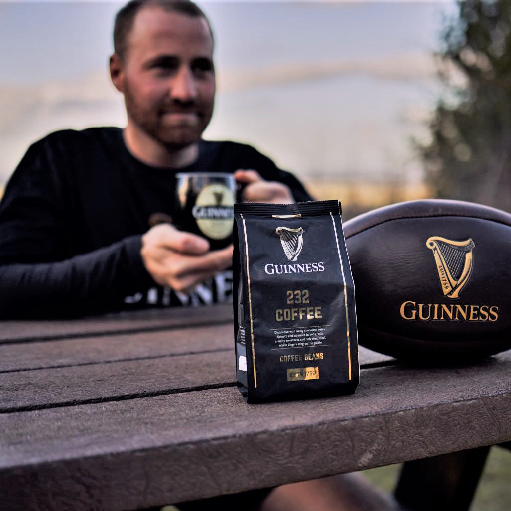 A man sitting on a picnic table with a bag of Guinness Coffee Beans 227g by Guinness.