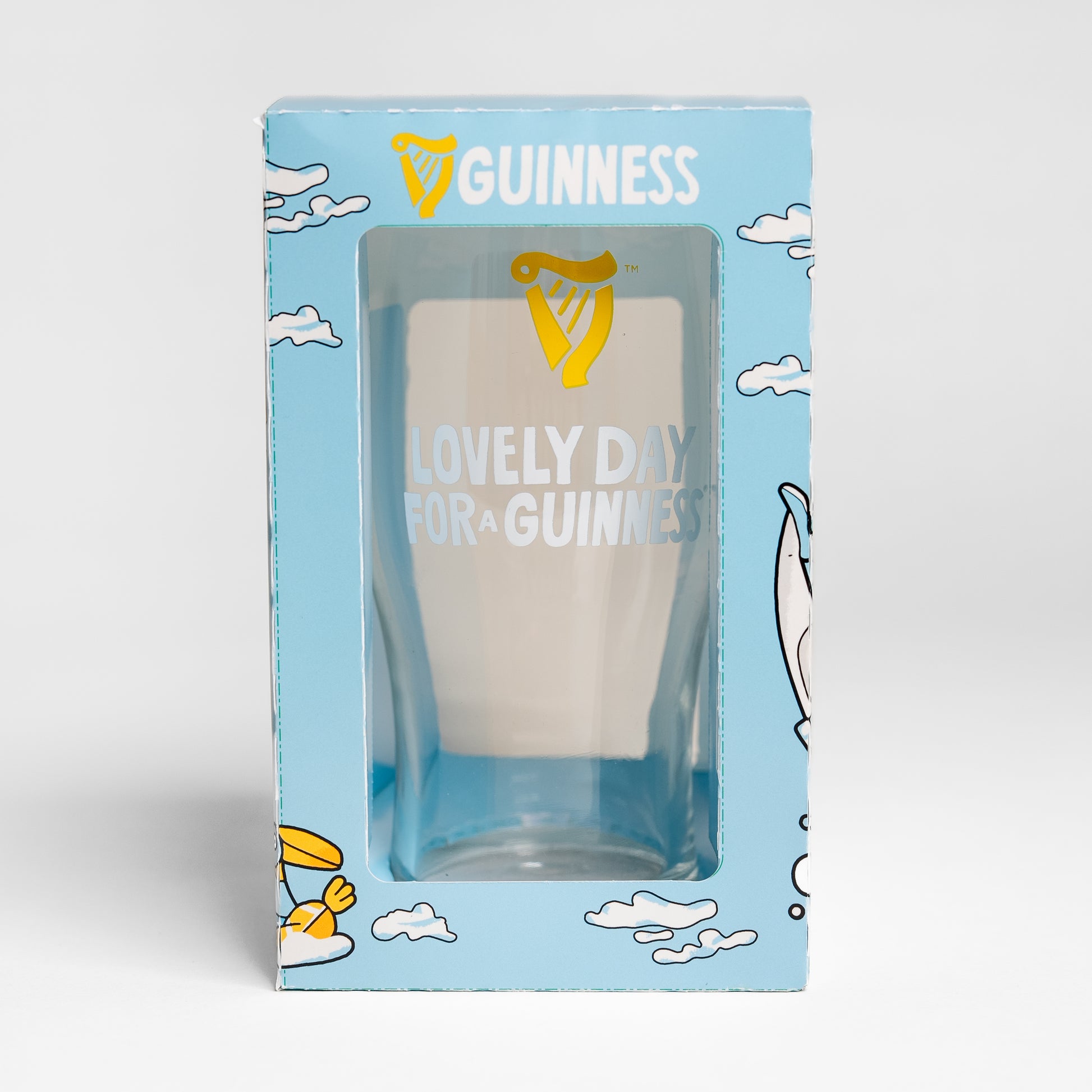 The Guinness Seb Curi Lovely Day Pint Glass from Guinness Webstore US features "Lovely Day for a Guinness" and the harp logo, packaged in a blue box with cloud and bird art by Sebastian Curi.