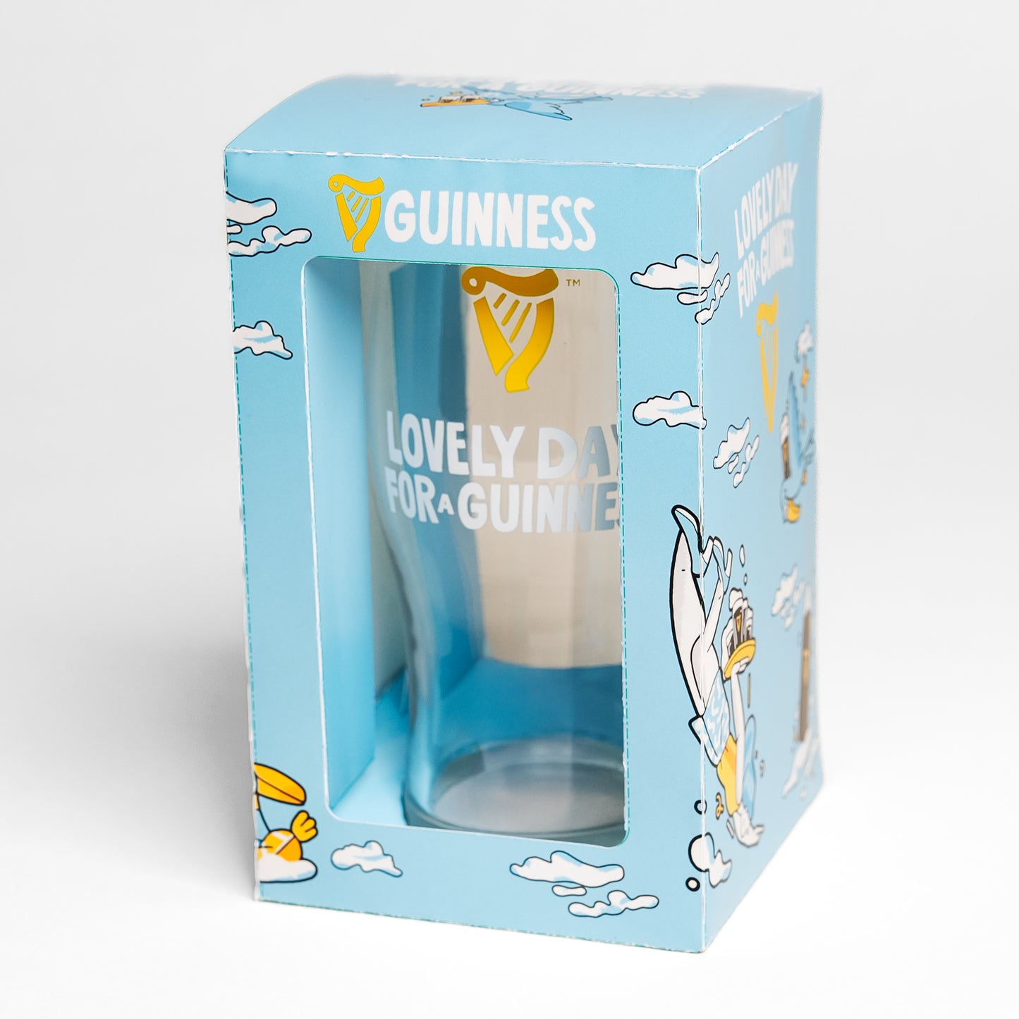 The Guinness Seb Curi Lovely Day Pint Glass from Guinness Webstore US comes in blue packaging with the "Lovely Day for a Guinness" slogan, cartoon clouds, and a toucan in Sebastian Curi's charming design.