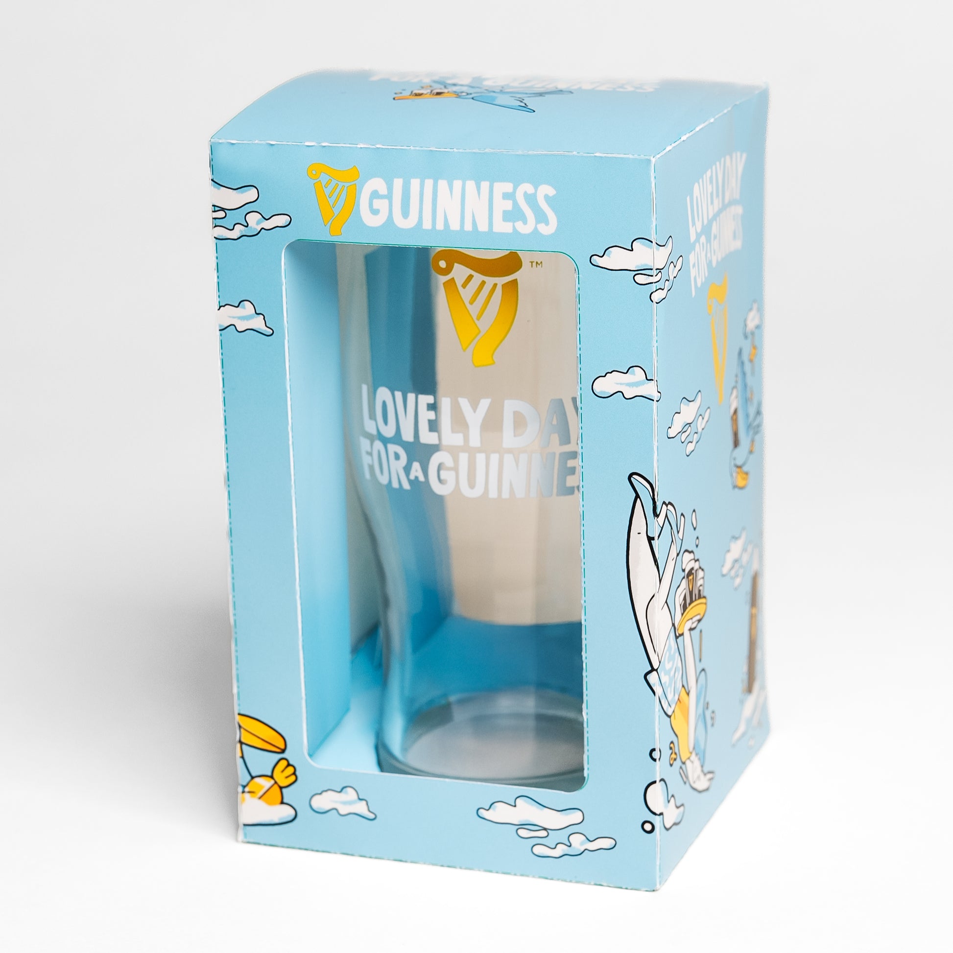 The Guinness Seb Curi Lovely Day Pint Glass from Guinness Webstore US comes in blue packaging with the "Lovely Day for a Guinness" slogan, cartoon clouds, and a toucan in Sebastian Curi's charming design.