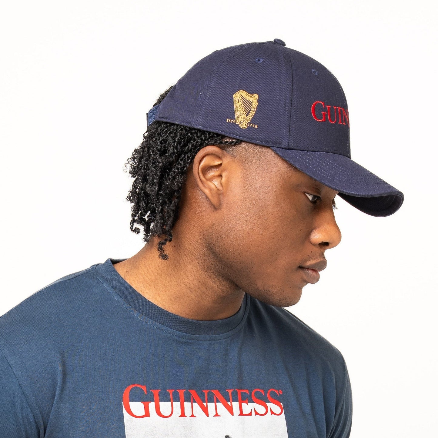 A person wearing a navy Guinness T-shirt with a vintage print and the timeless Guinness Transport Collection Baseball Cap by Guinness Webstore US, standing against a plain white background.