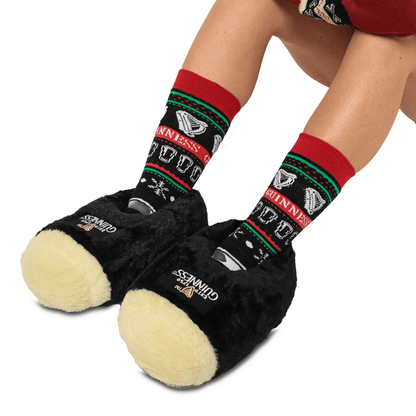 A woman wearing a pair of Guinness® Pint Slippers with a Christmas tree on them, featuring the unique Guinness Trademark Logo.