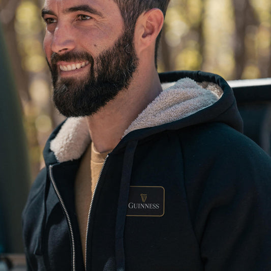 A cozy man wearing a Guinness Sherpa Lined Hoodie in the woods.
