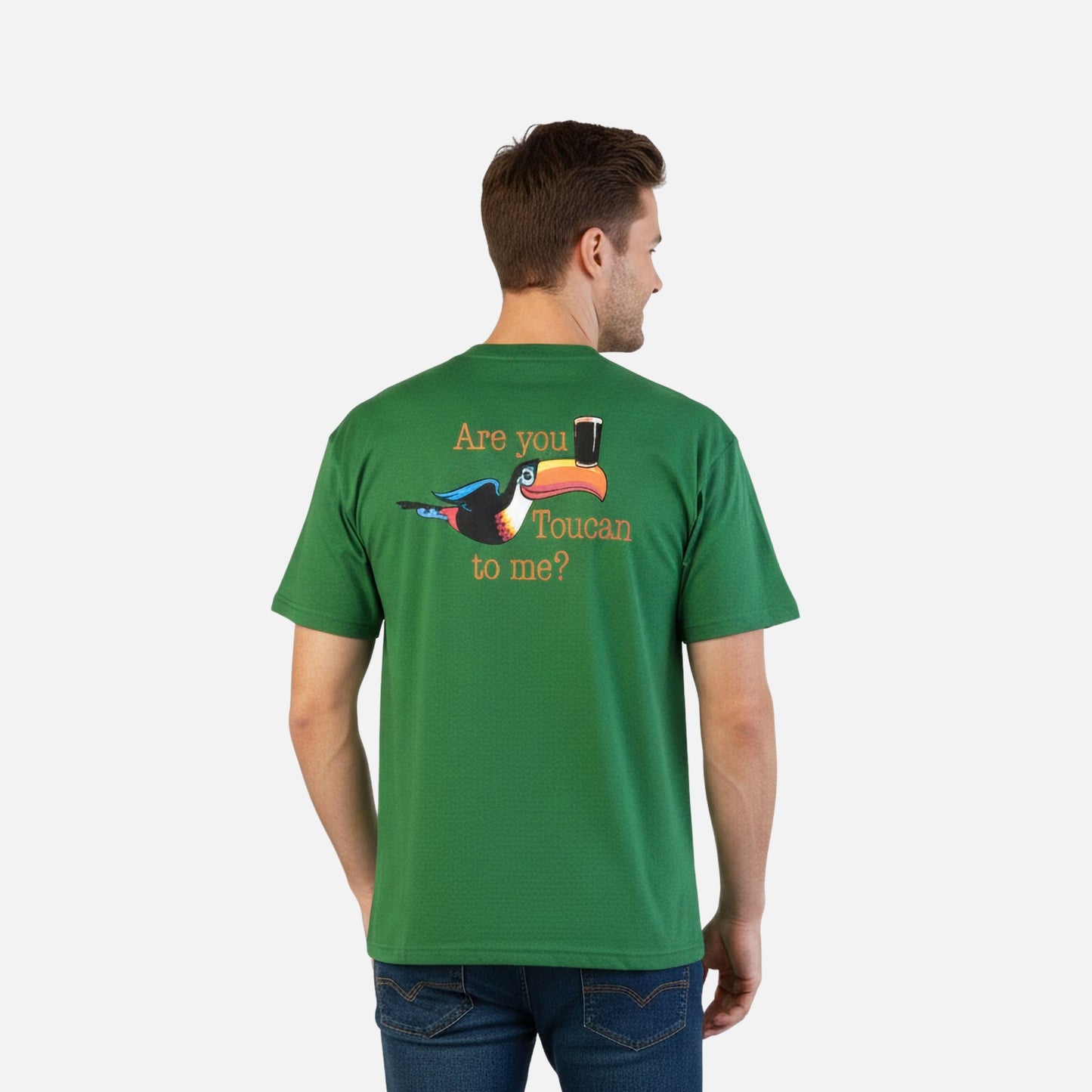 A man wears the Guinness Are you Toucan to Me Tee in green from Guinness Webstore US, made of BCI cotton and featuring a toucan graphic with a beer glass and "Are you Toucan to me?" on the back.