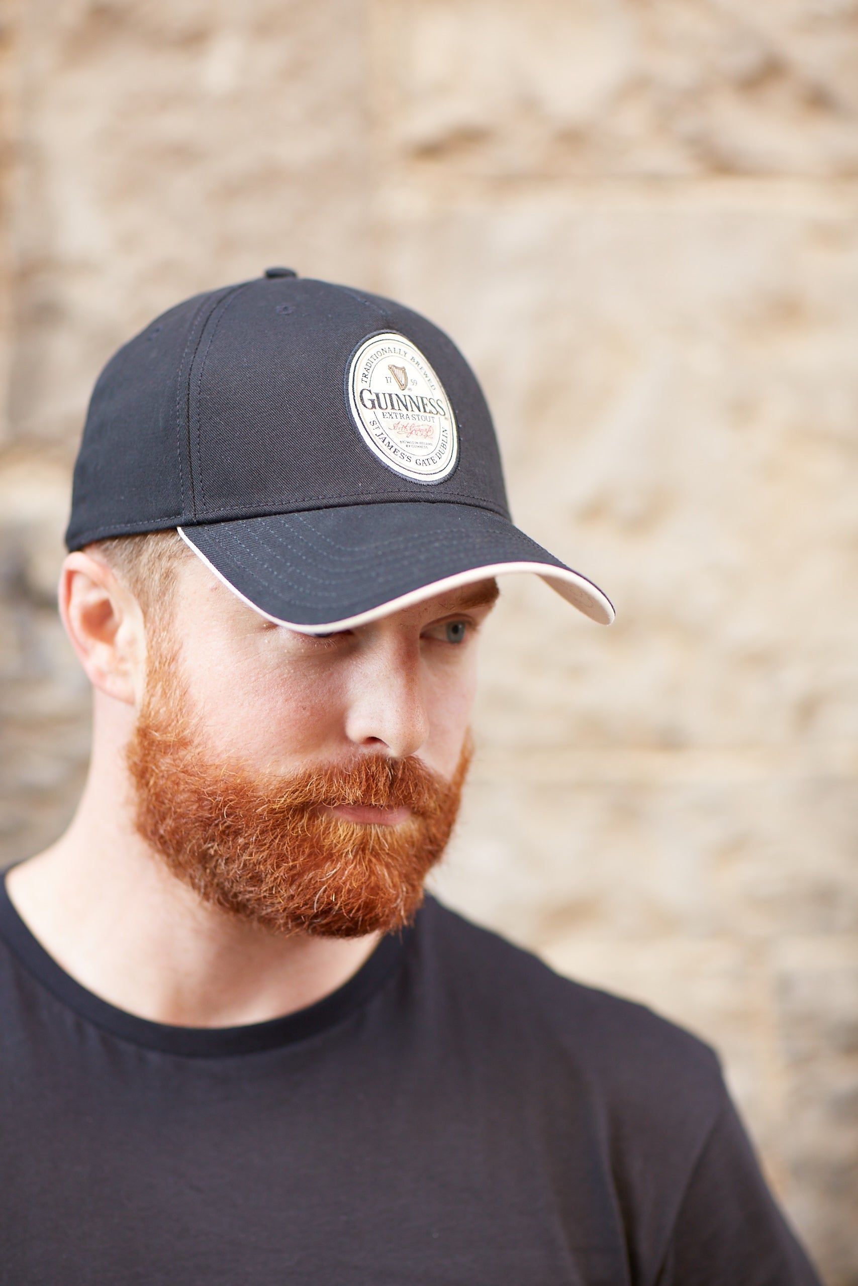 A Guinness fan sporting a Label Baseball Cap from his accessories collection, featuring a black hat with a vibrant red beard.