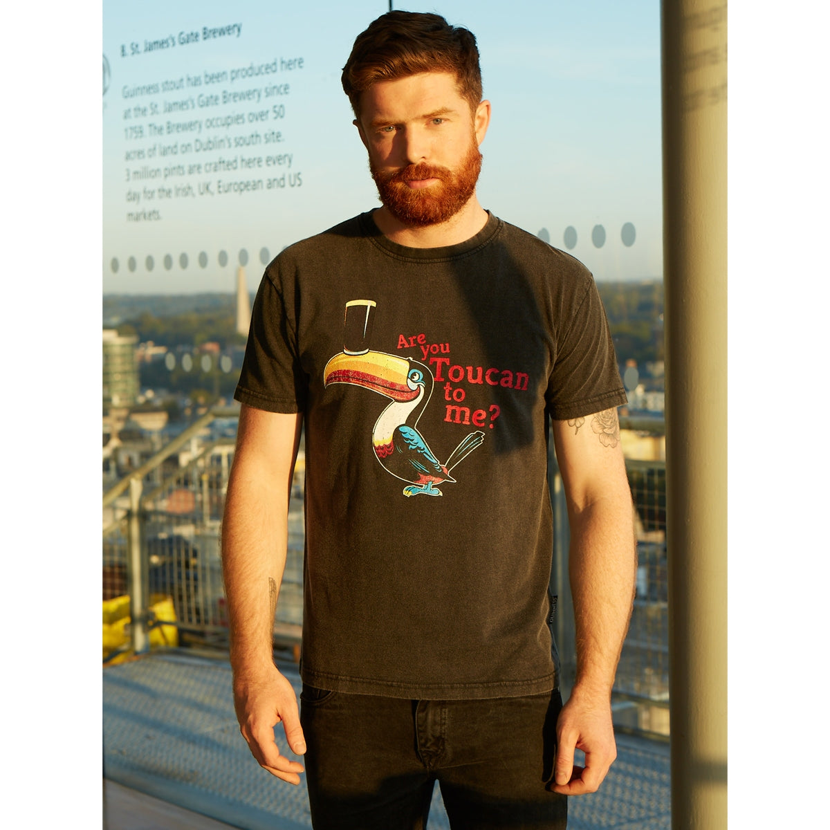 A man wearing a Guinness Are you Toucan to me Tee with a black t-shirt and a beard.