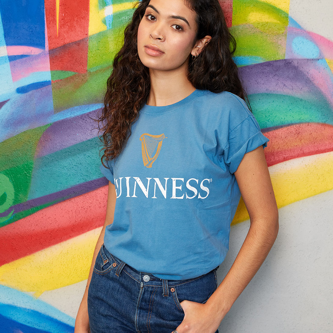 A woman donning a blue Guinness Trademark Label T-Shirt featuring the iconic trademark label.