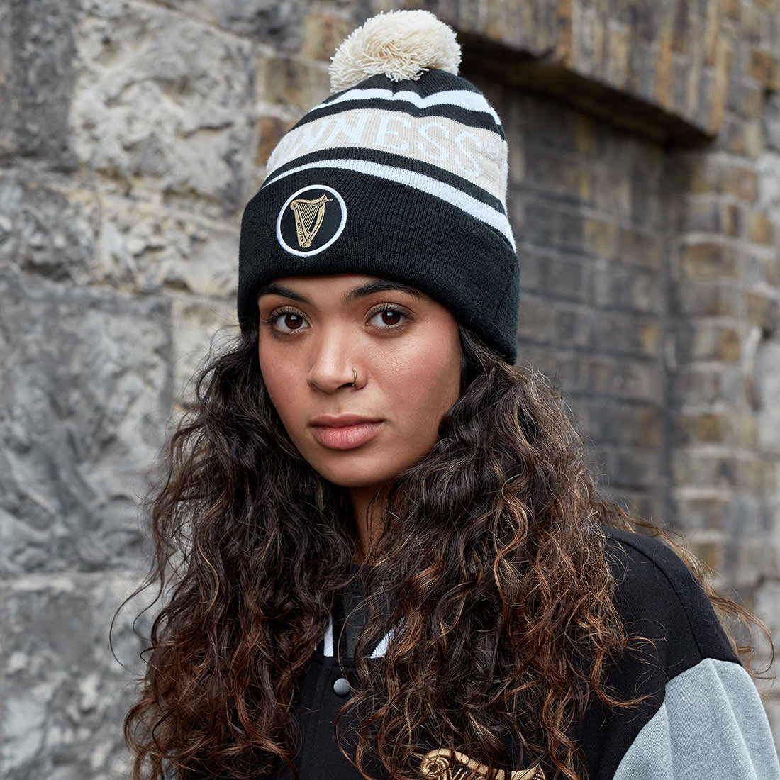 A young woman wearing a Guinness Black and White Premium Beanie, cozy with the Ireland flag on it.