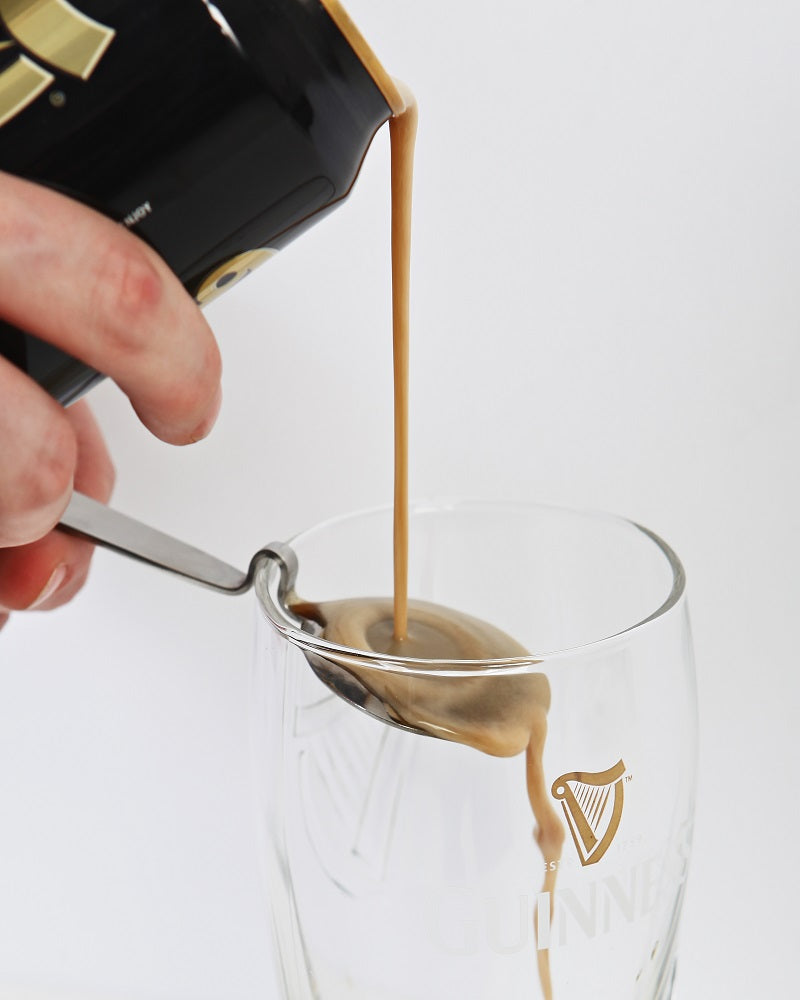 A person pouring a can of Guinness into a glass using a Guinness engraved pouring spoon.