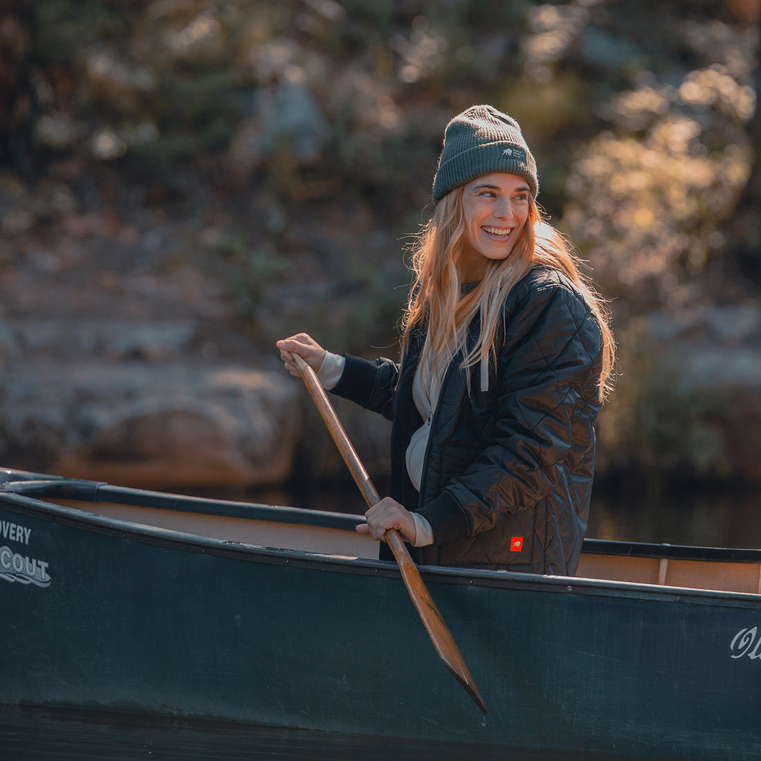 A woman in a waterproof green Guinness canoe with a beanie on her head.
