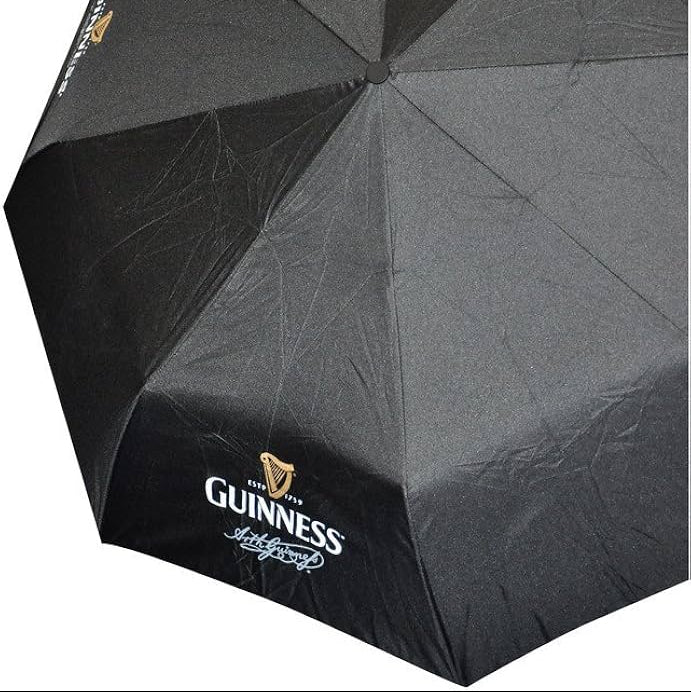 The Guinness Travel Umbrella is a black windproof umbrella featuring the white Guinness Trademark Logo and signature on several panels, offering reliable protection.