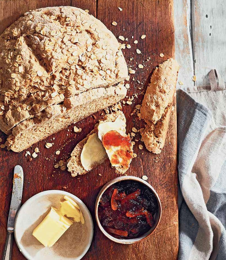 Traditional Irish soda bread recipe from the Official Guinness Hardcover Cookbook on a cutting board with butter and jam.