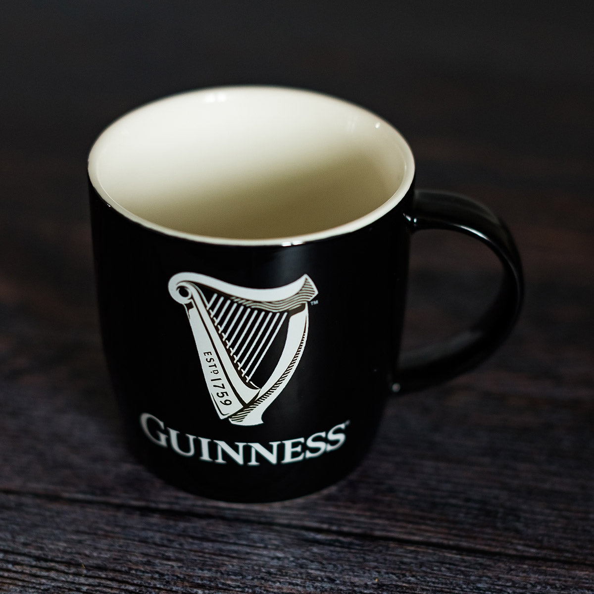 Guinness Black Mug with White Harp Logo resting on a sturdy wooden table.
