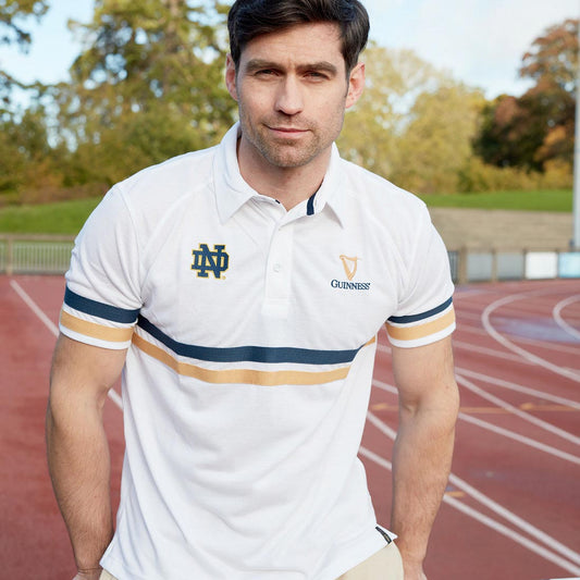 A man wearing a Guinness Notre Dame Performance Polo Shirt White standing on a track.