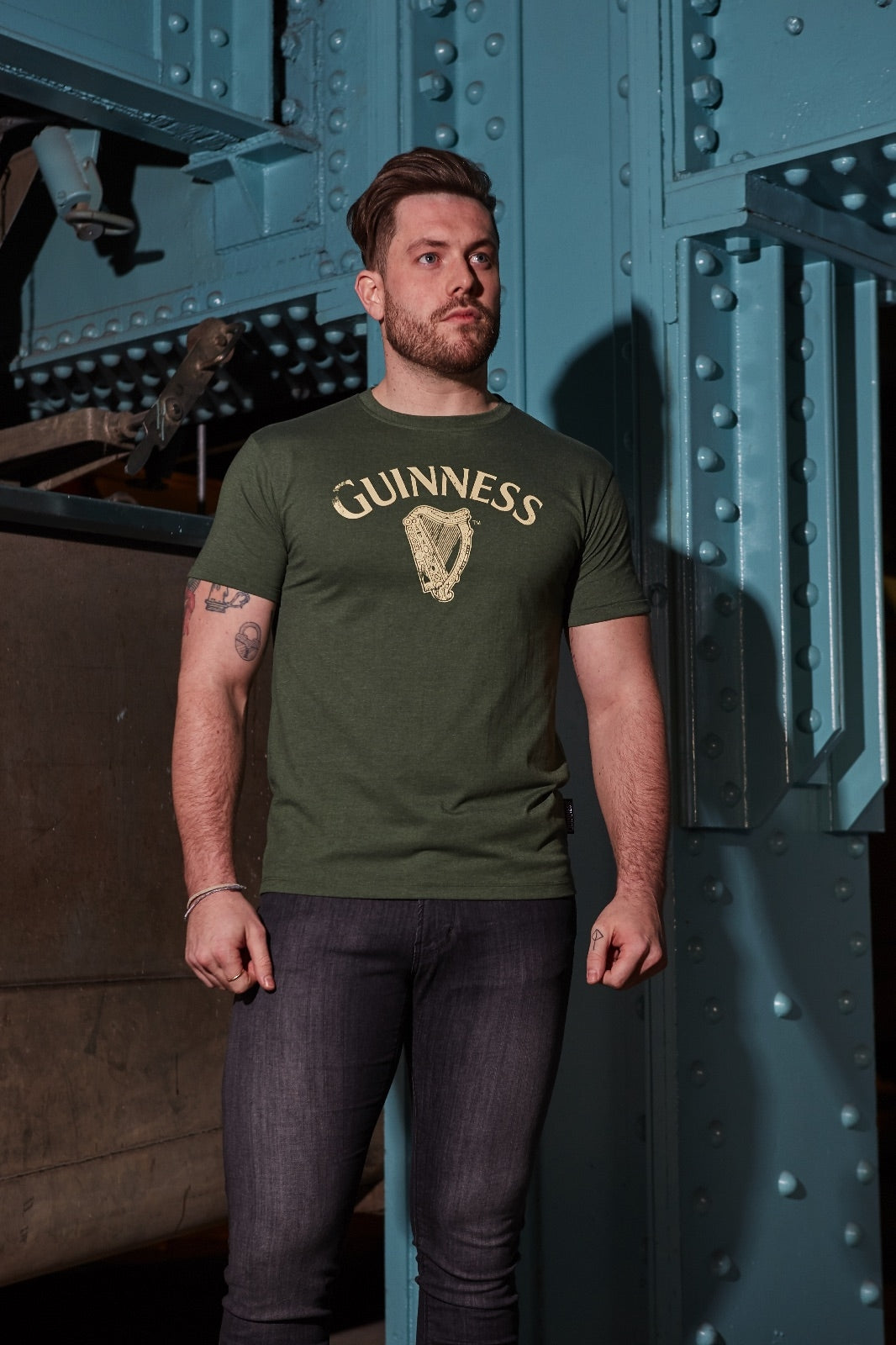 A man wearing a Guinness Vintage Harp Tee standing under a bridge.