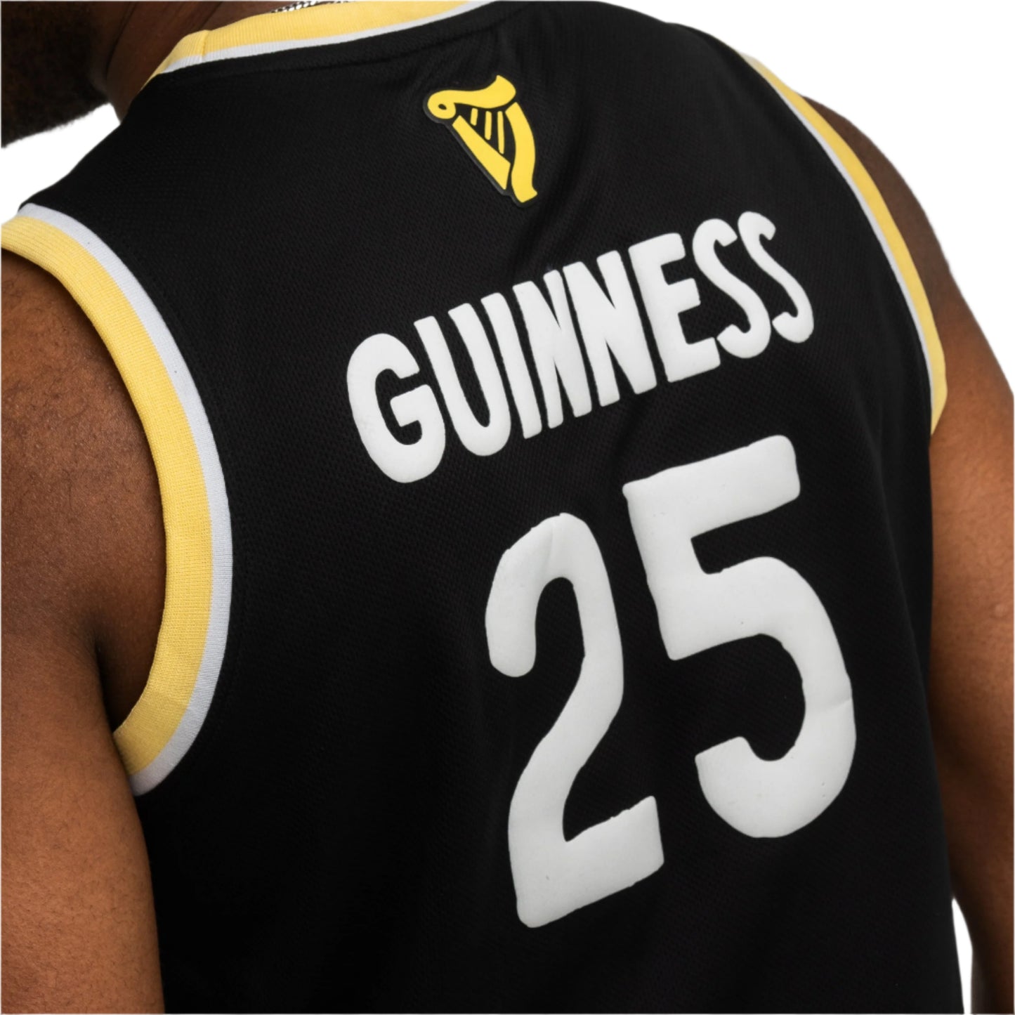 Close-up of a person in the Guinness Seb Curi Basketball Jersey from Guinness Webstore US—limited-edition black jersey with yellow and white trim, “Guinness” and 25 on back, plus harp logo. Part of the Sebastian Curi collaboration.