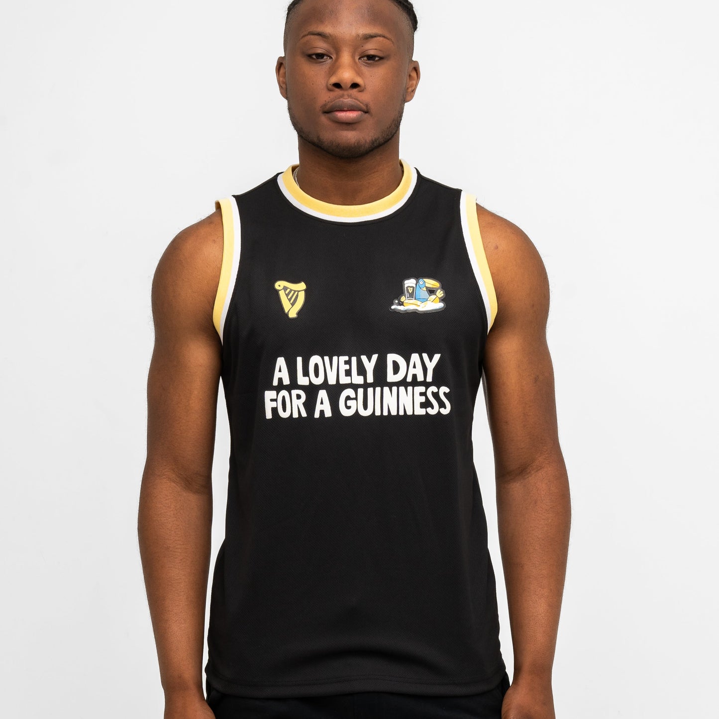 A person faces forward wearing the black sleeveless Guinness Seb Curi Basketball Jersey from Guinness Webstore US, featuring yellow trim and the phrase “A LOVELY DAY FOR A GUINNESS” on the front.
