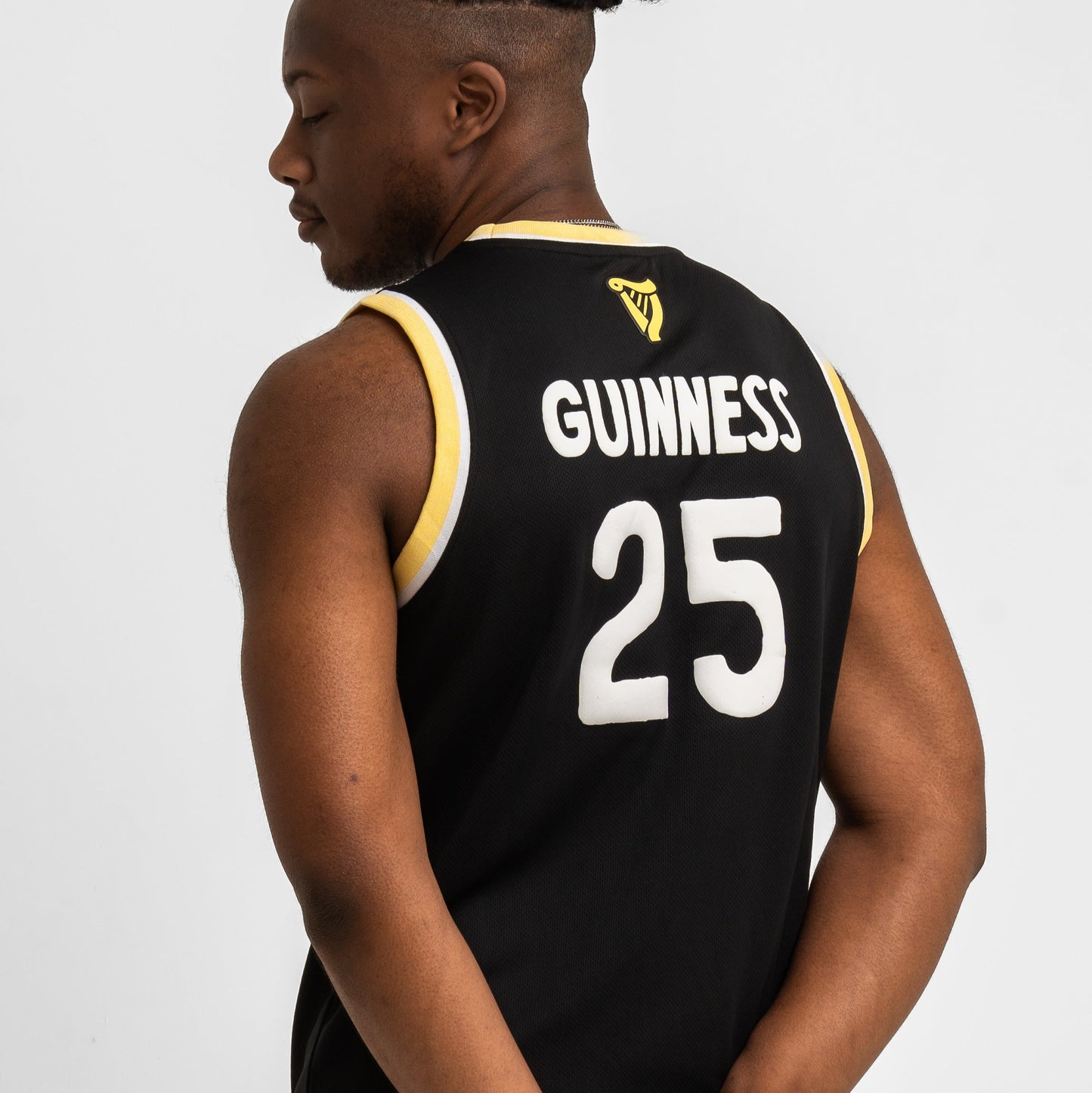 A man wears the Guinness Seb Curi Basketball Jersey from Guinness Webstore US—a black, sleeveless, limited-edition jersey with yellow trim, "GUINNESS" and the number 25 on the back.