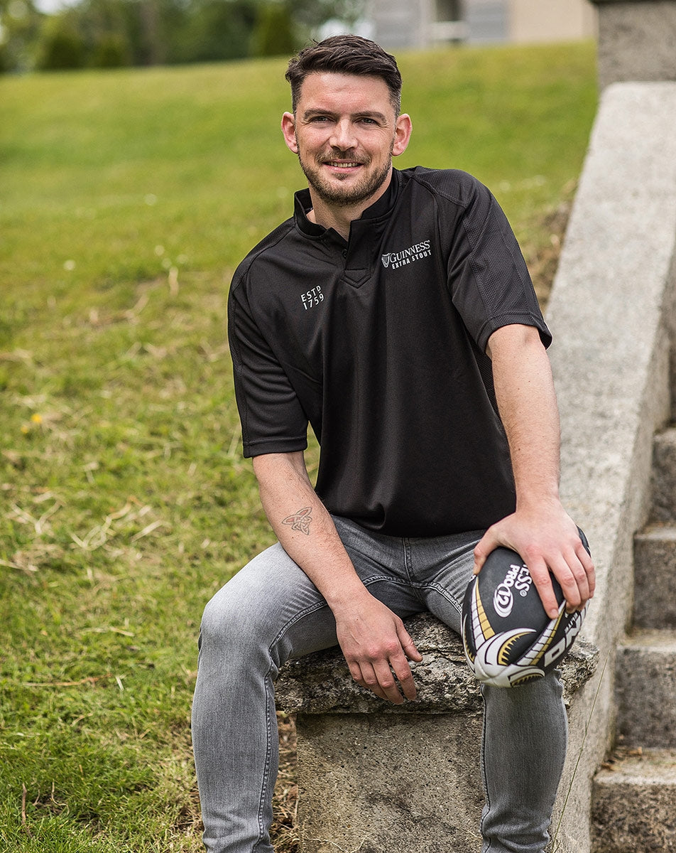 A man sitting on steps holding a Guinness All Black Rugby Jersey.