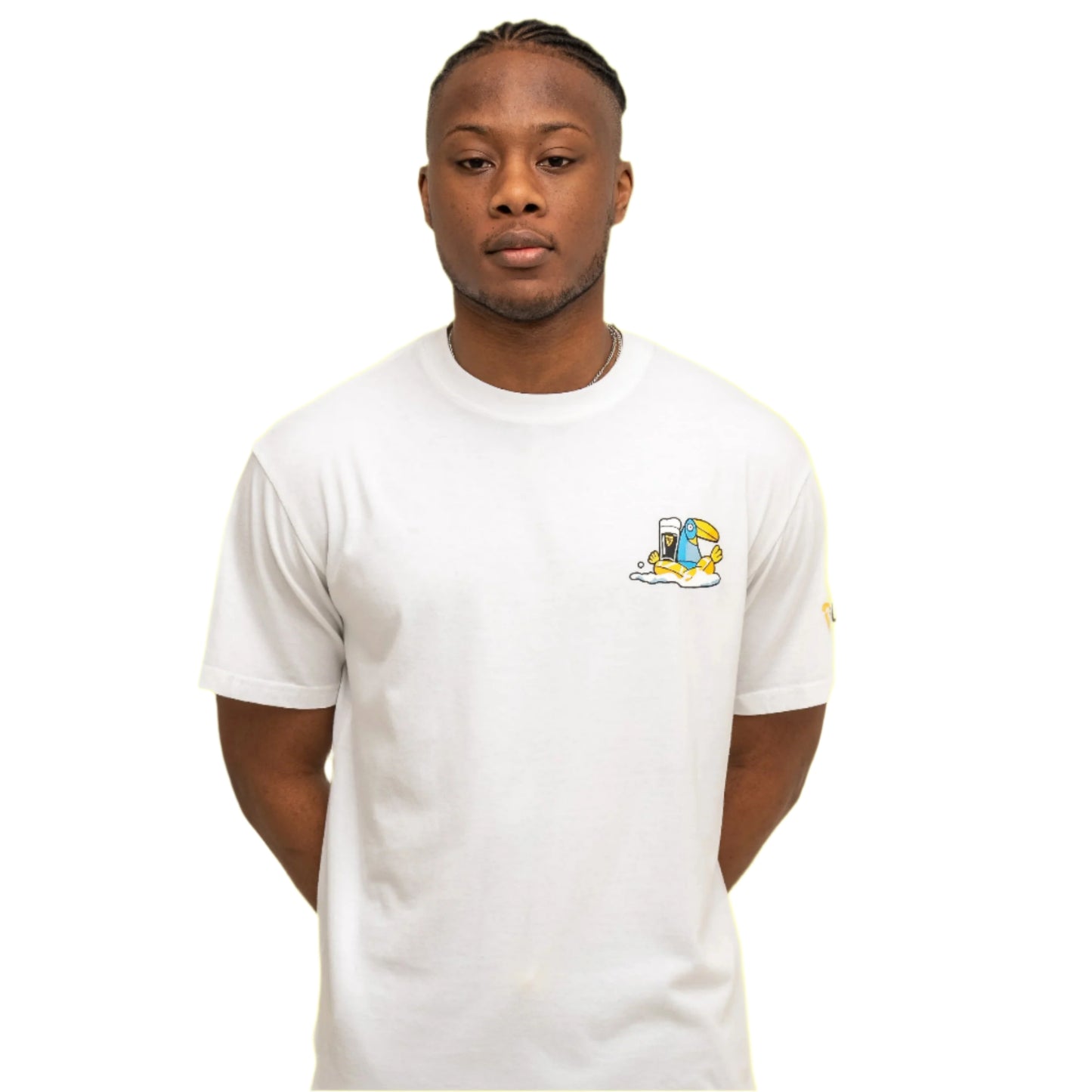 A person stands against a white background wearing the Guinness Webstore US Guinness Seb Curi Oversize Tee – White, featuring a small colorful cartoon graphic from the Sebastian Curi collaboration on the left chest.The tee has a small cartoon graphic of a blue toucan with a pint of Guinness on the chest