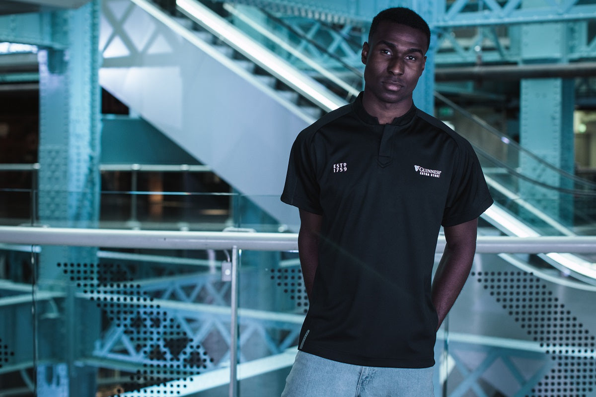 A man wearing an All Black Rugby Jersey with Guinness branding stands on an escalator.