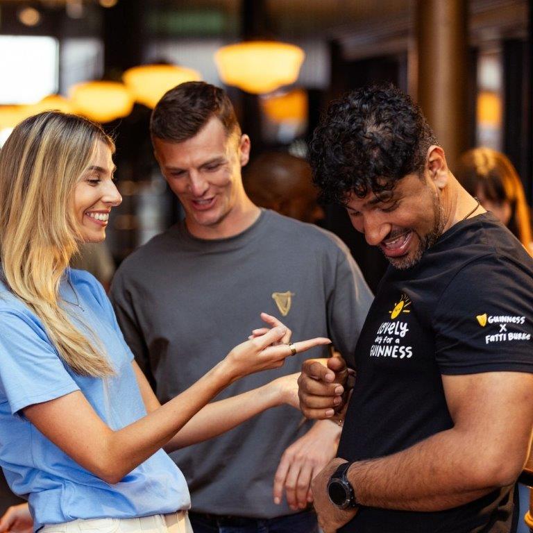 A group of people wearing Guinness t-shirts talking to each other in a bar during summer.