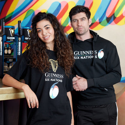 A man and a woman wearing Guinness hoodies stand in front of a colorful promotional backdrop.