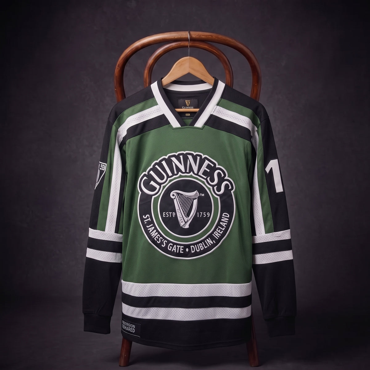 A Guinness Green & White Hockey Jersey with black accents, featuring the classic “Guinness” brand name and iconic harp logo on the front, as well as the number 17 on the sleeve, is displayed on a chair against a dark background. This bold and distinctive jersey highlights tradition for fans of both hockey and Guinness.