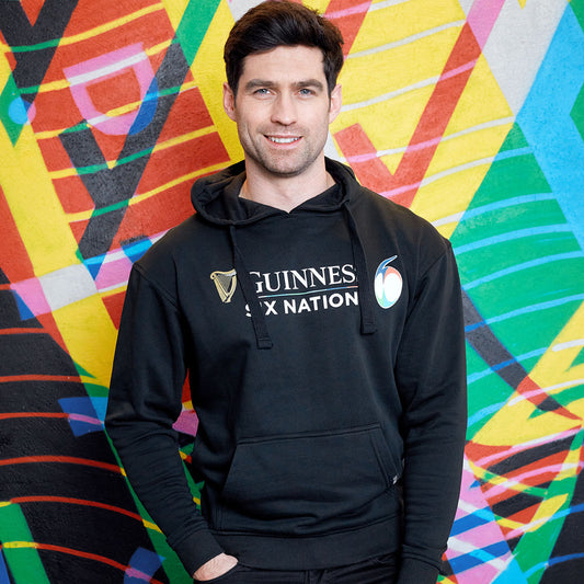 Man in a Guinness Six Nations Rugby Hoodie smiling in front of a colorful abstract mural.