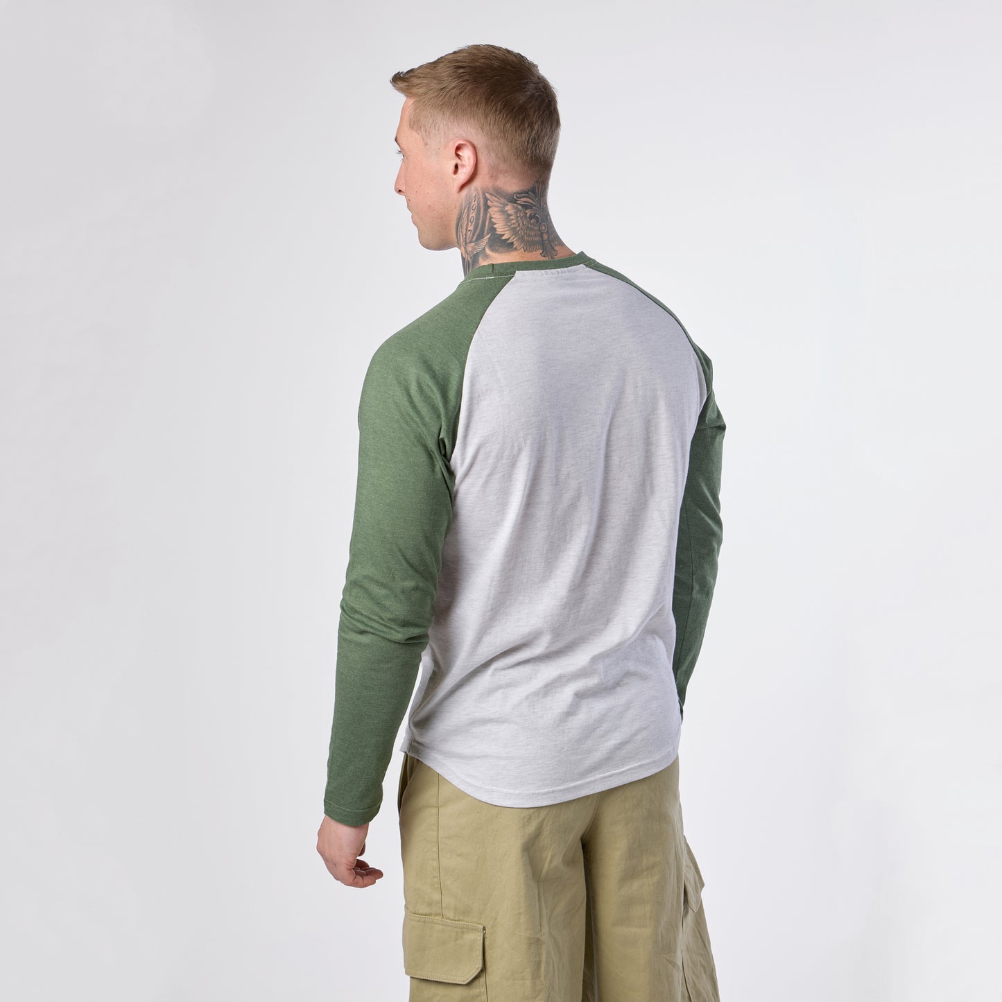 A man with a neck tattoo, wearing the Guinness Baseball T-Shirt by Guinness and khaki cargo shorts, stands facing away against a plain white background.