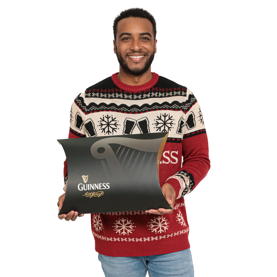 A smiling man in a holiday sweater holds a large pillow-shaped Guinness Clothing Gift Box.