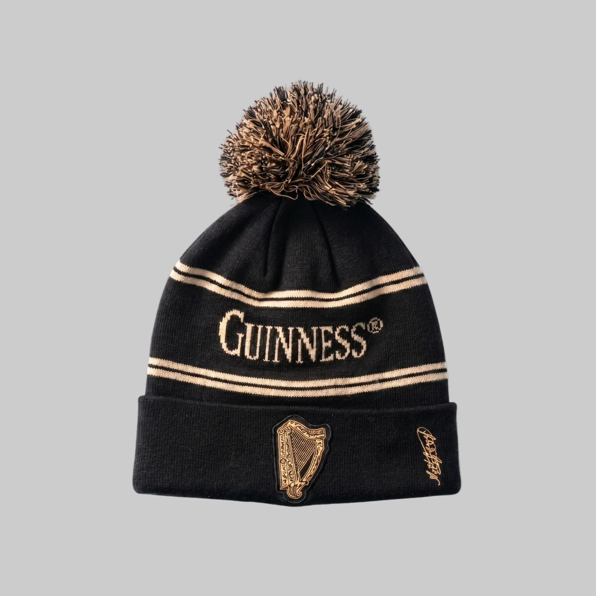 The Guinness Black & Gold Sports Beanie – Vintage Harp Knit features gold stripes, a large pom-pom, "Guinness" text, a vintage harp design, and a signature of founder Arthur Guinness on the folded brim.