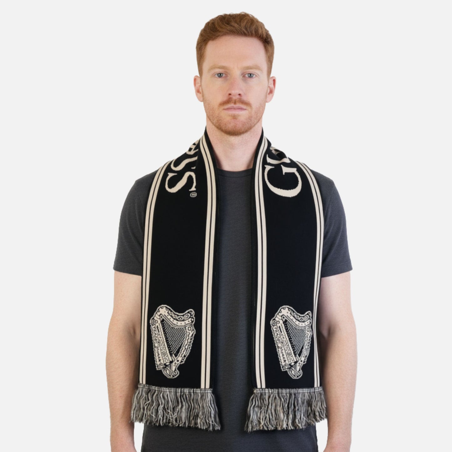 A man with short red hair wears a black t-shirt and the Guinness Black & Gold Sports Scarf – Vintage Harp Knit, featuring fringed ends.