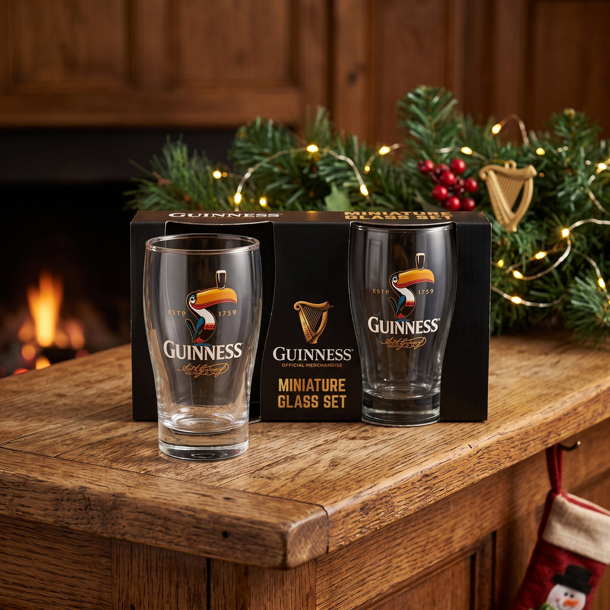 Two Guinness Toucan Mini Pint Glasses from Guinness Webstore US in front of the box—festive décor and a fireplace make this collectible set perfect for any fan.