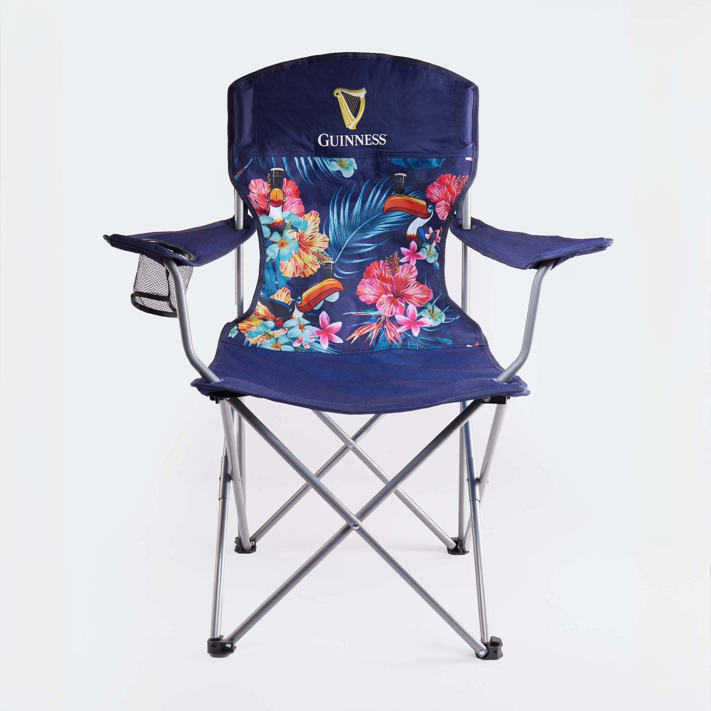 The Guinness Toucan Hawaiian Beach Chair from Guinness Webstore US features metal legs, a vibrant floral and leaf print backrest with the classic toucan logo, plus a mesh cup holder—making it a must-have beach essential.