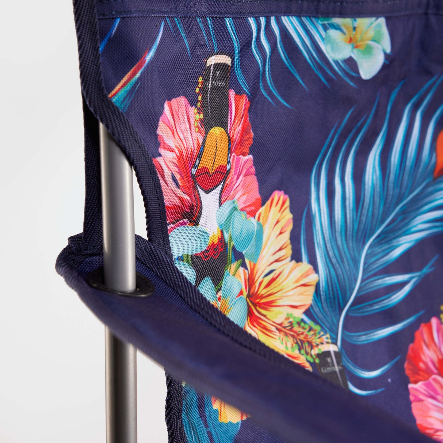 Close-up of the Guinness Toucan Hawaiian Beach Chair by Guinness Webstore US, featuring tropical floral fabric with bottles on a metal frame—a foldable, must-have accessory for relaxing outdoors at the beach.