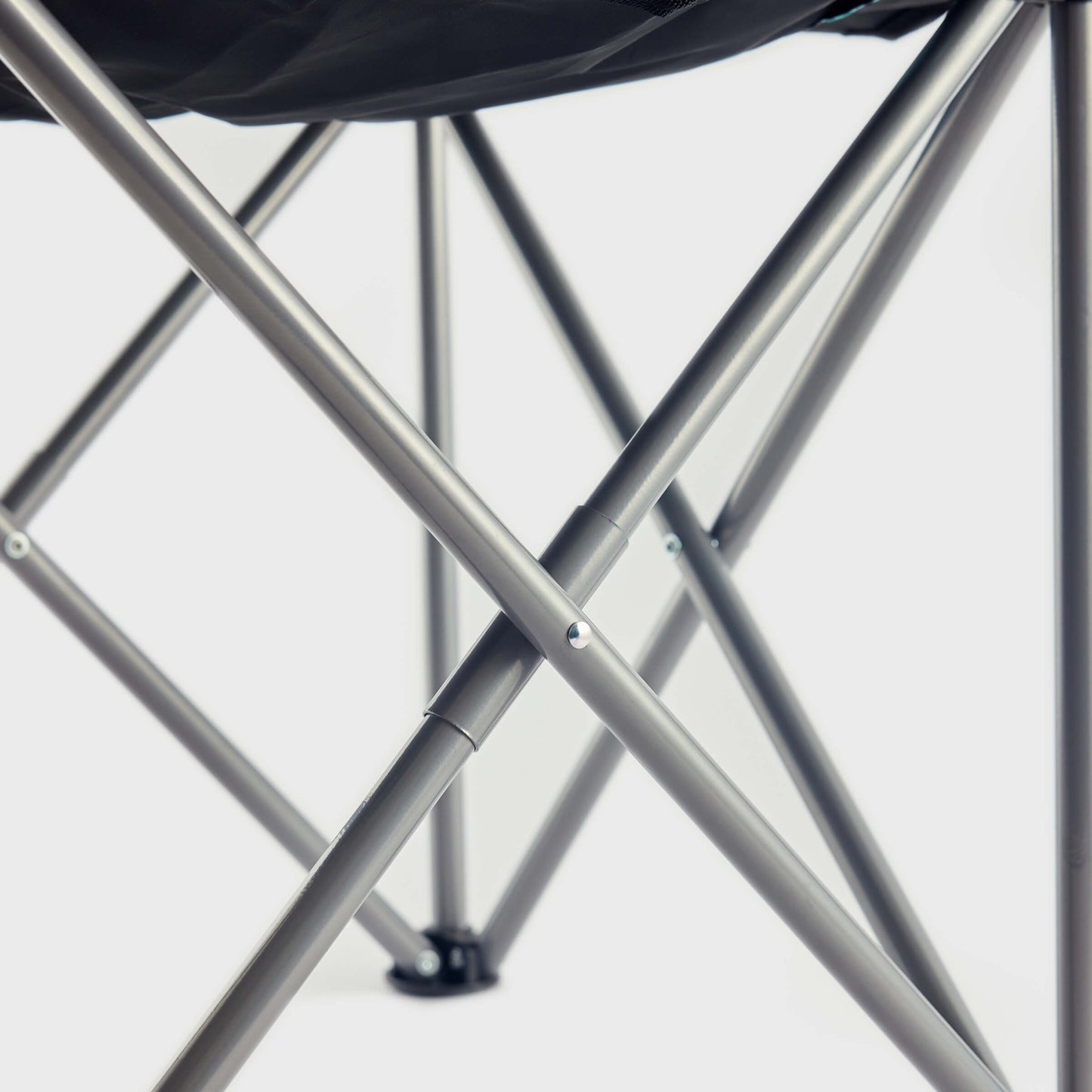 Close-up of the crossed metal legs on the Guinness x Fatti Burke Hawaiian Camping Chair by Guinness, featuring a vibrant Hawaiian design draped over the seat, set against a plain white background.