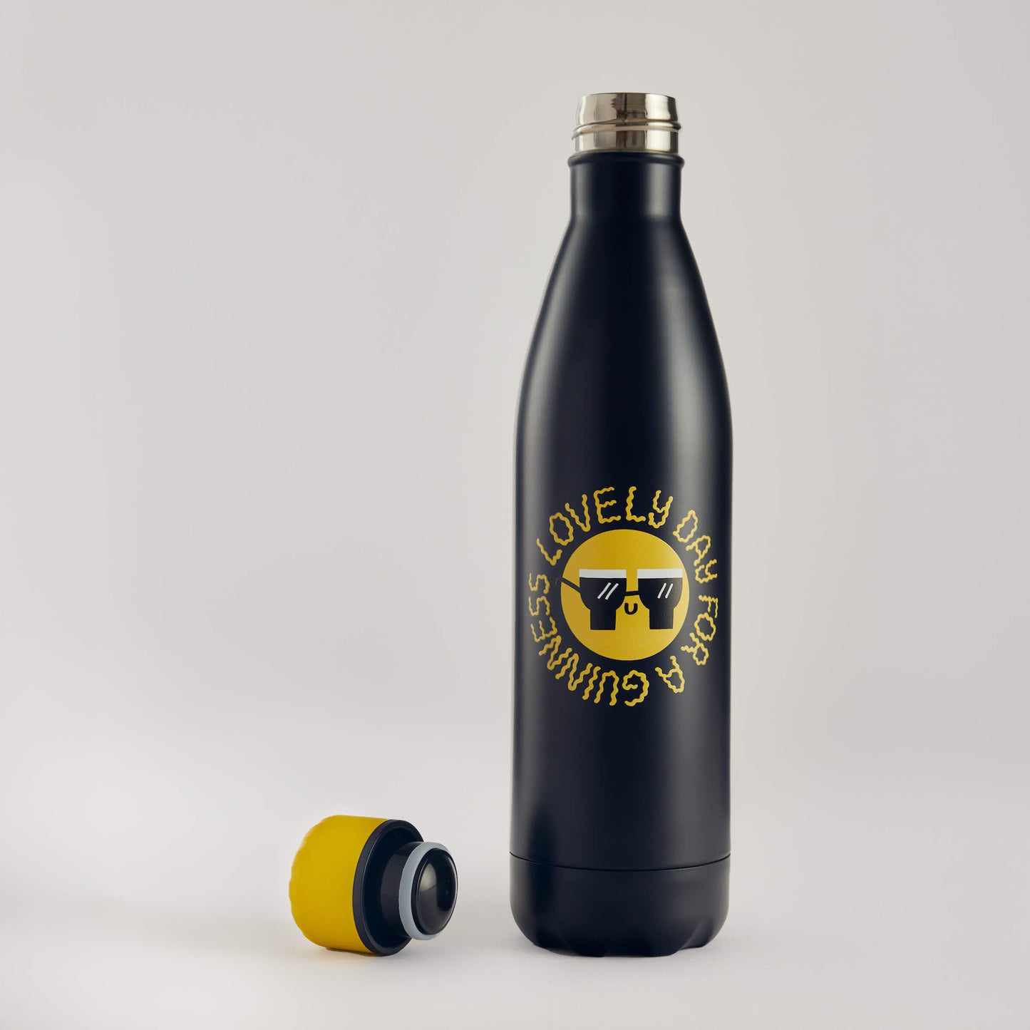 The Guinness x Fatti Burke Sun Water Bottle is a black stainless steel, BPA-free bottle with a yellow and black cap, featuring “LOVELY DAY FOR A GUINNESS” and sunglasses, from the Guinness Hawaiian collection.