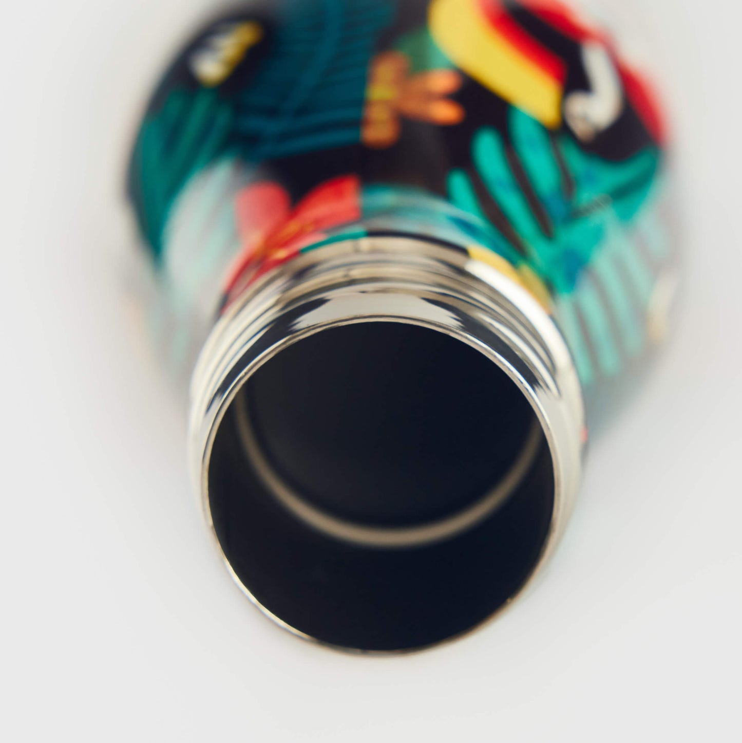 Close-up of the open mouth of the Guinness x Fatti Burke Hawaiian Water Bottle by Guinness, featuring a colorful tropical leaf and toucan design on stainless steel.