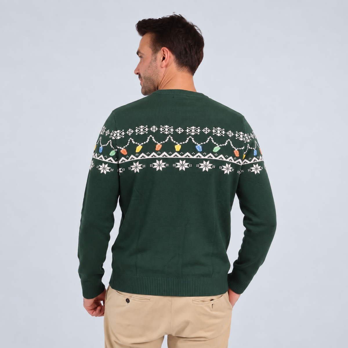A man wearing the Guinness Holiday Pint Lights Sweater in green from Guinness Webstore US, featuring a festive white and colorful pattern, stands with his back to the camera against a light background.
