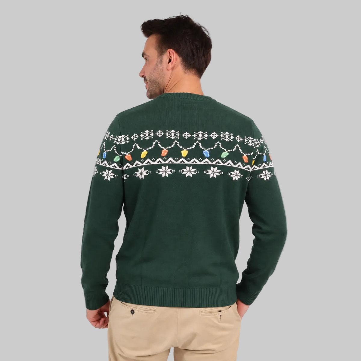 A man wearing the Guinness Holiday Pint Lights Sweater in green from Guinness Webstore US, featuring a festive white and colorful pattern, stands with his back to the camera against a light background.