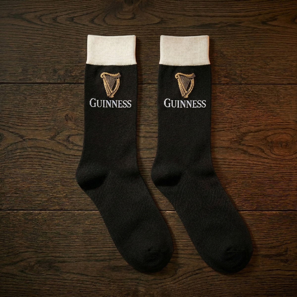Guinness Pint Crew Socks – Black, featuring the iconic logo and harp, make an ideal Guinness gift, stylishly displayed on a wooden surface.
